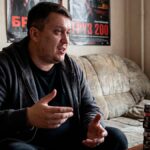 Евгений Зайферт в спортивной кофте сидит на сером диване